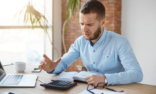 Portrait of unhappy mature bearded accountant working in company office, being frustrated calculating profits one more time because of mistake. Business concept